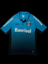 Camisa de futebol Umbro X Grêmio 2015 azul e preta com logo do time e patrocinador Banrisul. Detalhe de listras "Tramontina" nas mangas.