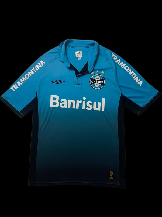 Camisa de futebol Umbro X Grêmio 2015 azul e preta com logo do time e patrocinador Banrisul. Detalhe de listras "Tramontina" nas mangas.