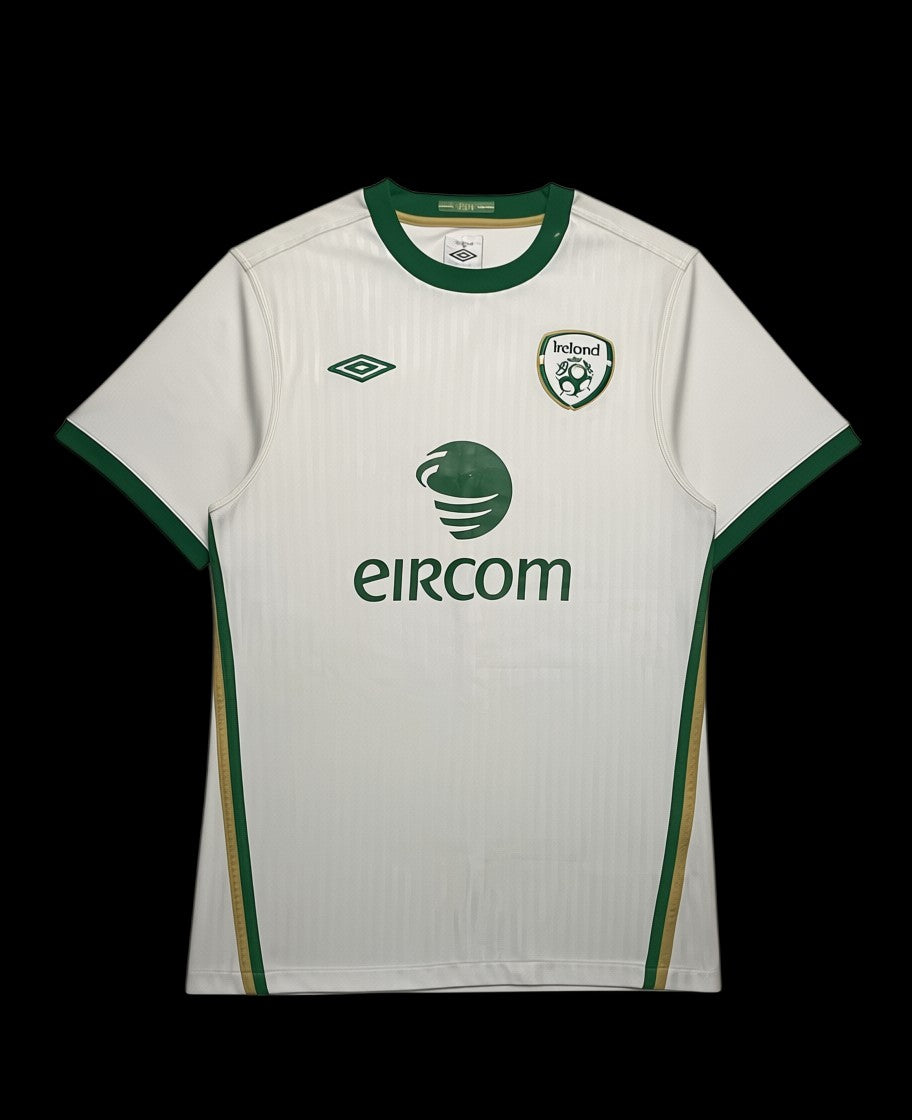Camisa de futebol branca da Irlanda 2010 da Umbro com detalhes verdes e dourados. Logo da Irlanda e patrocínio Eircom.