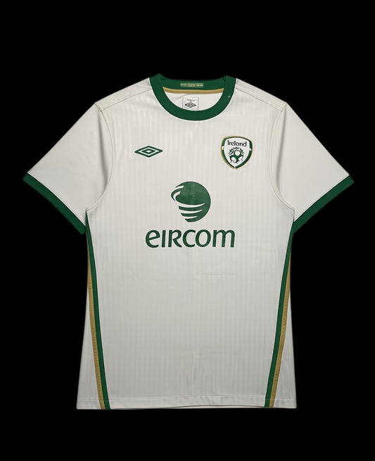 Camisa de futebol branca da Irlanda 2010 da Umbro com detalhes verdes e dourados. Logo da Irlanda e patrocínio Eircom.