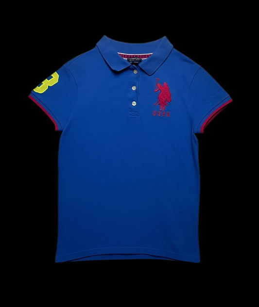 Camisa polo feminina azul royal da USPA com logo rosa, número 8 amarelo na manga e detalhes em rosa nas barras da manga e gola.