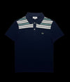 Camisa polo masculina azul marinho da Lacoste com listras verdes e brancas na gola e peito, logo do crocodilo bordado.