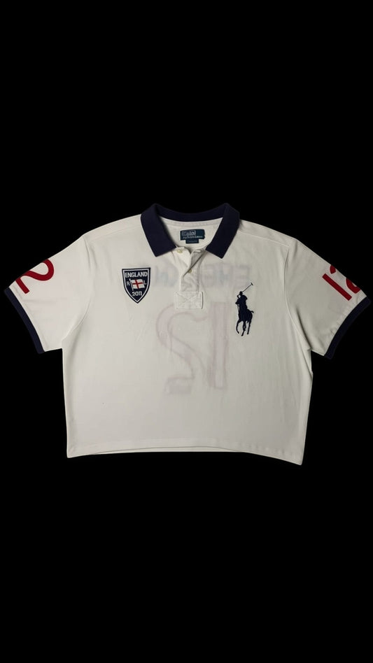 Polo cropped branco da garimpo do madruga com gola azul marinho, logo do cavalo e jogador de polo bordado, escudo da Inglaterra e número 12 nas mangas. Peça de upcycling.