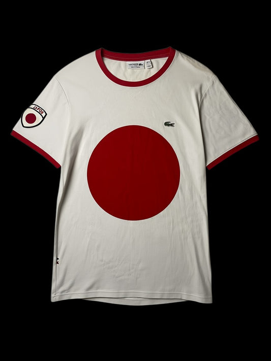 Camisa branca masculina Lacoste Japão Edição Especial com gola e punhos vermelhos. Estampa frontal de círculo vermelho e detalhe de bandeira do Japão na manga.